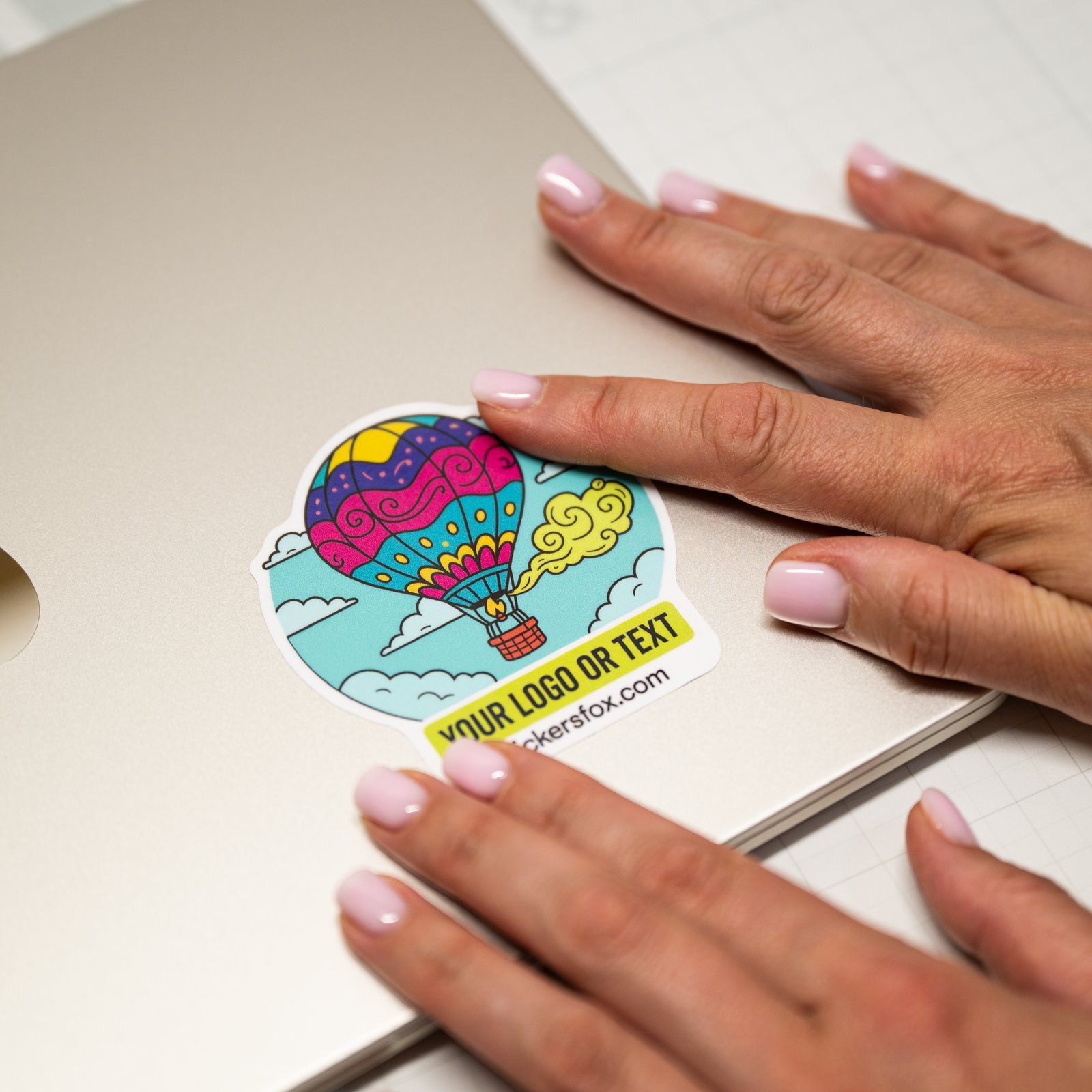 A custom die-cut sticker being smoothed onto a laptop lid by hand