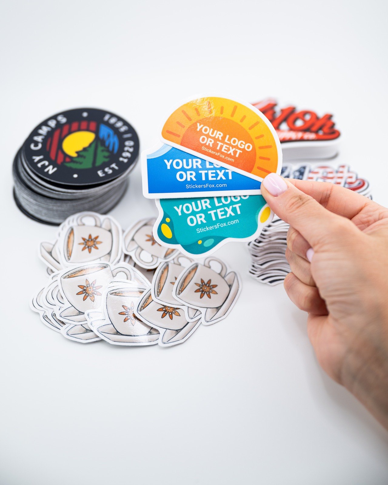 Custom die-cut logo stickers held above a fresh order of printed stickers
